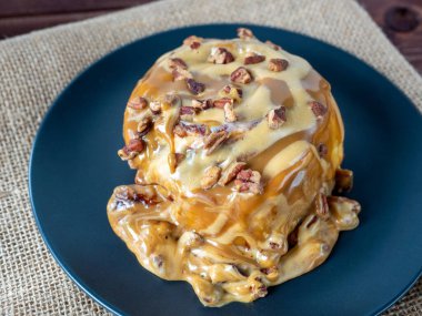 Karamel soslu ve cevizli tarçınlı çöreğin yakın çekimi. Siyah tabak, keten peçete. Üst manzara, düz uzanma