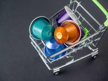 Aromatik öğütülmüş kahveyle dolu renkli alüminyum kapsüllerle dolu küçük bir market arabası. Modern kahve depolama ve hazırlama teknolojileri. Siyah arkaplan.