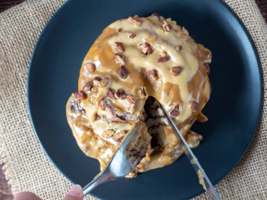 Karamelli ve fındıkla süslenmiş tarçınlı çöreğin yakın çekimi siyah bir tabak ve keten peçeteyle süslenir, tatlı çatal ve bıçakla kesilir. Üst manzara, düz uzanma