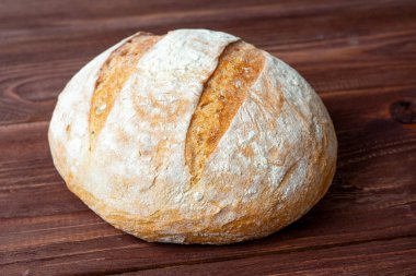 Kahverengi ahşap arka planda duran yuvarlak bir somun ekmeğin yakın çekimi. Fırın, fırın konsepti. Yan görünüm