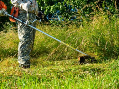 Benzin biçme makinesi kullanan bir adam uzun otlar keser. Yaz. Kırsal alan, bölgenin bakımı.
