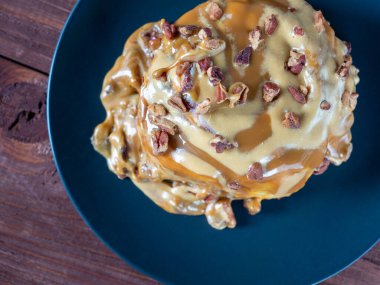 Tatlı, lezzetli bir tatlı fındıklı tarçınlı çörek ve üzerine karamel sosu serpiştirilmiş siyah bir tabak ve dışkı. Üst görünüm düzlüğü