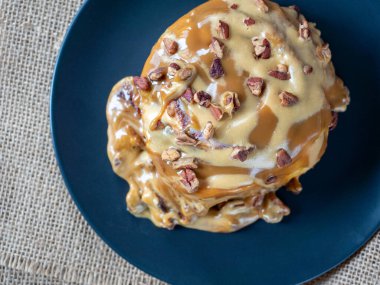 Karamel soslu ve cevizli tarçınlı çöreğin yakın çekimi. Siyah tabak, keten peçete. Üst manzara, düz uzanma