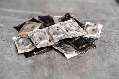 Gri arkaplandaki prezervatiflerin en üst görüntüsü. Gümüş ve siyah folyo ambalaj kauçuk prezervatif arka planı.
