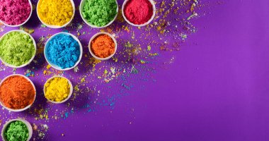 Mutlu Holi Festivali dekorasyonu. Mor arkaplandaki renkli holi tozunun üst görüntüsü. Metin için kopya alanı da var..