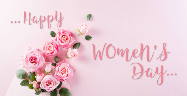 Happy Women's Day concept. Top view of roses flowers, heart and "Happy Women's Day" text on pink pastel background.