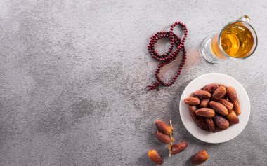 Ramazan Kareem dekorasyonunun en üst görüntüsü, koyu taş zemin üzerinde meyve, çay ve tespih tarihleri.
