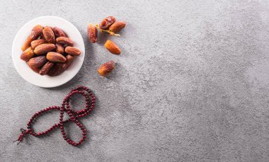 Ramazan Kareem dekorasyonunun üst görünümü, koyu taş zemin üzerinde meyve ve tespih tarihleri.