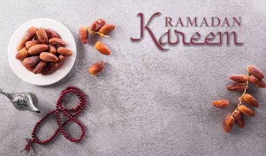 Ramazan Kareem dekorasyonunun üst görünümü, meyveler, çay ve koyu taştan arkaplanda yazılı tespih taşları.