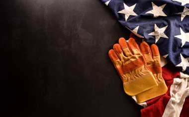 İşçi Bayramı konseptin kutlu olsun. Koyu taş zemin üzerinde farklı inşaat araçları bulunan Amerikan bayrağı.