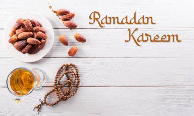 Ramazan Kareem dekorasyonunun en üstteki görüntüsü, beyaz ahşap zemin üzerine yazılmış olan meyve ve tespih tanelerinin tarihleri.