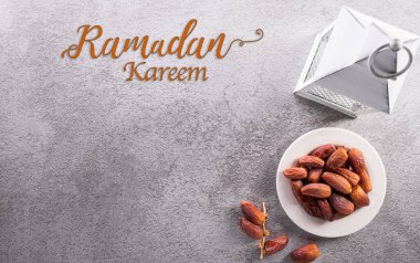 Ramazan Kareem dekorasyonunun üst görünümü, koyu taş arkaplanda metni bulunan meyve ve Arap lambası tarihleri.