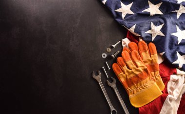 İşçi Bayramı konseptin kutlu olsun. Koyu taş zemin üzerinde farklı inşaat araçları bulunan Amerikan bayrağı.