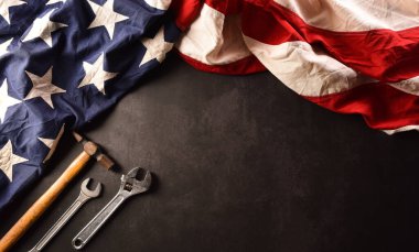 İşçi Bayramı konseptin kutlu olsun. Koyu taş zemin üzerinde farklı inşaat araçları bulunan Amerikan bayrağı.