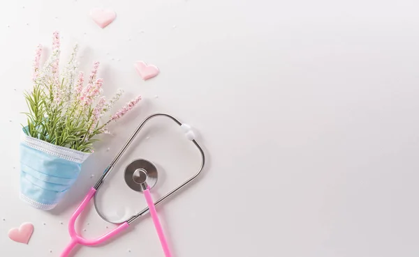 Top view of doctor stethoscope, medical mask and flowers on white background. International nurse day and medical concept.