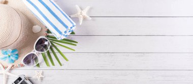 Yaz tatili, seyahat ve tatil konsepti. Güneş gözlüğü, denizyıldızı, plaj şapkası, parmak arası terlik, eski kamera ve beyaz ahşap arka planda deniz kabuğu..