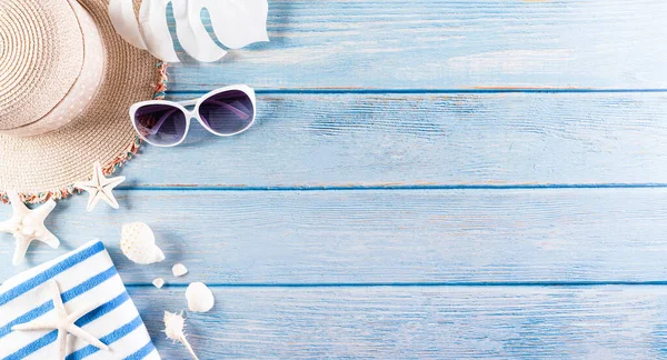 Yaz tatili, seyahat ve tatil konsepti. Güneş gözlüğü, denizyıldızı, plaj şapkası, parmak arası terlik ve pastel mavi ahşap arka planda deniz kabuğu..