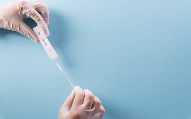 Doktorun elinde mavi arka planda kovid 19 hızlı antijen testi var. Dünya çapında koronavirüs salgını konsepti.