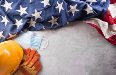 Coronavirus hastalığı (Covid-19) sırasındaki İşçi Bayramı konseptin kutlu olsun. Koyu taş arka planda farklı inşaat araçları ve tıbbi maskeli Amerikan bayrağı.