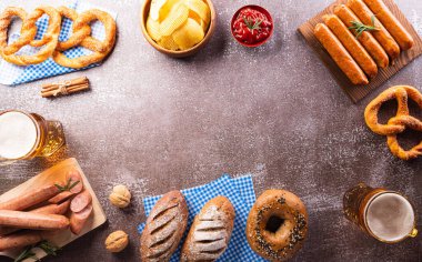Oktoberfest festival decoration symbols made from Pretzel loaf, beer, sausage, potato chips and Bavarian white and blue fabric on dark stone background.
