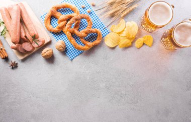Oktoberfest festival decoration symbols made from Pretzel loaf, beer, sausage, potato chips and Bavarian white and blue fabric on stone background.