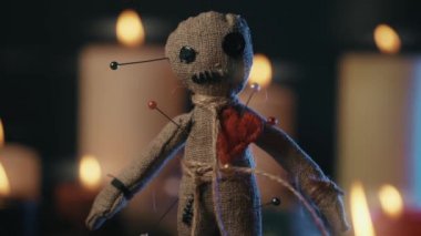Vudu büyüsü konsepti. Voodoo bebeği iğnelerle süslenmiş, kalbi delinmiş ve mumların etrafında yanan bir bebek. Ürkütücü ya da ürkütücü büyülü ezoterik ritüel