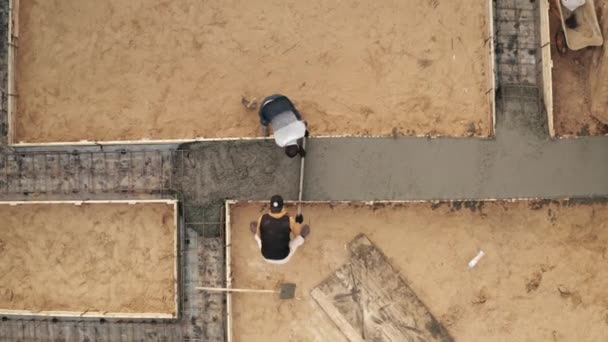 Рабочие выравнивание жидкого бетона или цемента на армирование стали, строительство фундамента здания в процессе, вид сверху с воздуха — стоковое видео
