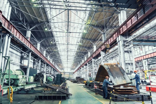 Innenraum einer metallurgischen Anlage. Große Werkstatt mit Metallbearbeitungsmaschinen. Arbeiter in Masken laden Bleche auf Kran ab — Stockfoto