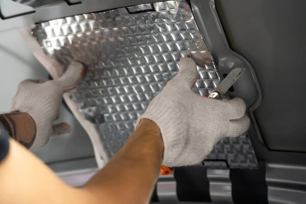 Worker hands glues soundproofing material to inside of car hood. Process of car sound insulation installation