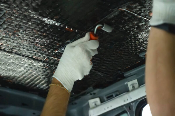 Worker hand rolls sound-insulating material with roller for better adhesion. Soundproofing for car