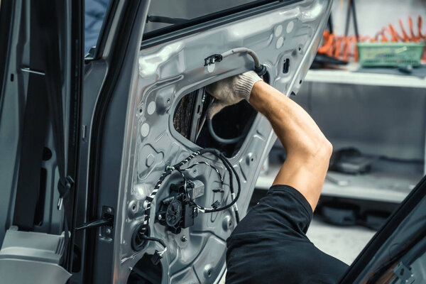 Auto service worker disassembles car door for repair, restoration, tuning car sound or installing noise insulation or soundproofing