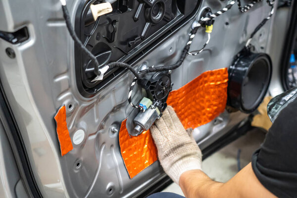 Worker installing special acoustic and vibration-damping material for noise insulation on car door. Soundproofing, auto tuning