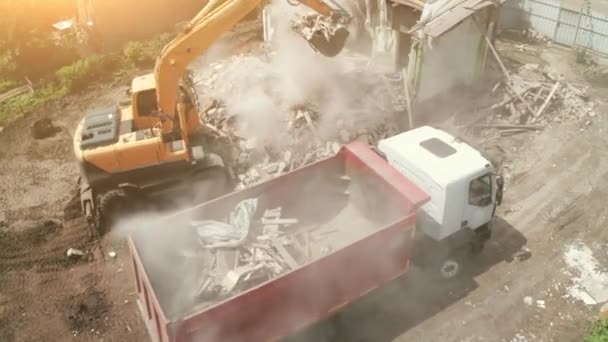Démolition du bâtiment. Excavatrice charge les déchets de construction dans le camion pour le retrait du chantier de construction, vue aérienne — Video
