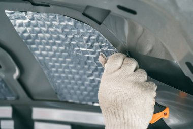 İşçi kaputun içine ses yalıtımı malzemesi yapıştırıyor. Araba ses yalıtım kurulumu süreci