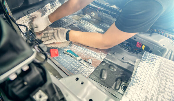 Auto service worker installs soundproofing material inside car interior, soundproofing insulation