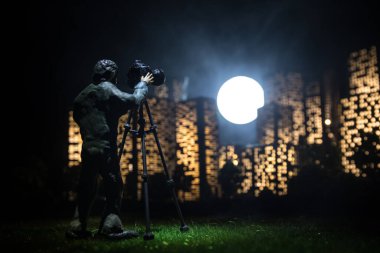 Çizgi film tarzı şehir binaları. Minyatür şehrin gece çekimleri için tripodlu dijital kamera. Geceleri kameralı bir fotoğrafçı. Seçici odak.