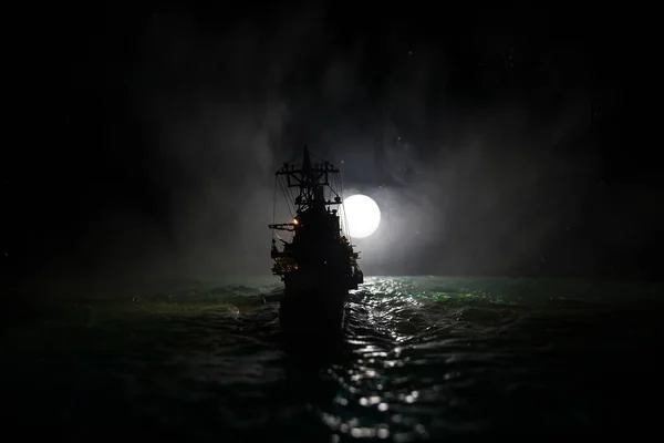 War concept. Night battle scene at sea. Dramatic moon decorated effect. Silhouette of the battle ship in night. Miniature creative table decoration. Selective focus
