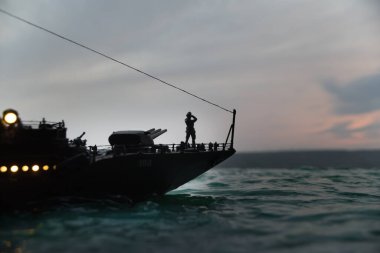 Savaş konsepti. Denizde gece savaşı sahnesi. Dramatik tonlu bulut etkisi. Gün batımında savaş gemisinin silueti. Minyatür yaratıcı masa dekorasyonu. Seçici odak