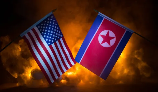 USA and North Korea flags on burning dark background. Concept of crisis of war and political conflicts between nations. Selective focus