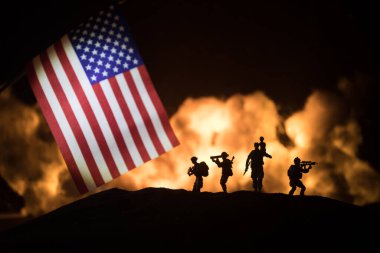 Yanan karanlık arka planda ABD bayrağı. Savaş krizi kavramı ve uluslar arasındaki siyasi çatışmalar. Amerikan bayrağına karşı silahlı asker silueti. Seçici odak