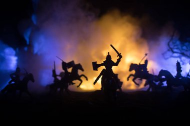 Süvari ve piyadelerle ortaçağ savaş sahnesi. Şekillerin siluetleri ayrı nesneler olarak, karanlık tonlu sisli arka planda ortaçağ şatosuyla savaşan savaşçılar arasında. Seçici odak