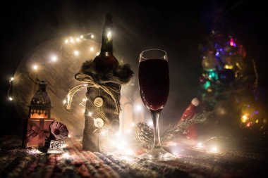 Noel süslemeli bir kadeh şarap. Kırmızı şarap kristal bardakta, renkli halıda şişe ve yaratıcı yeni yıl süslemeleri. Boşluğu kopyala