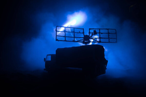 Creative artwork decoration. Silhouette of mobile air defence truck with radar antenna at night. Rocket launcher aimed at sky ready to attack. Selective focus