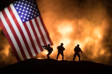 US small flag on burning dark background. Concept of crisis of war and political conflicts between nations. Silhouette of armed soldier against a USA flag. Selective focus clipart