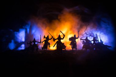 Süvari ve piyadelerle ortaçağ savaş sahnesi. Şekillerin siluetleri ayrı nesneler olarak, karanlık tonlu sisli arka planda ortaçağ şatosuyla savaşan savaşçılar arasında. Seçici odak