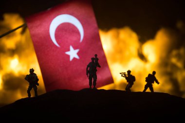 Yanan karanlık arka planda küçük bir hindi bayrağı. Savaş krizi kavramı ve uluslar arasındaki siyasi çatışmalar. Türk bayrağına karşı silahlı asker silueti. Seçici odak