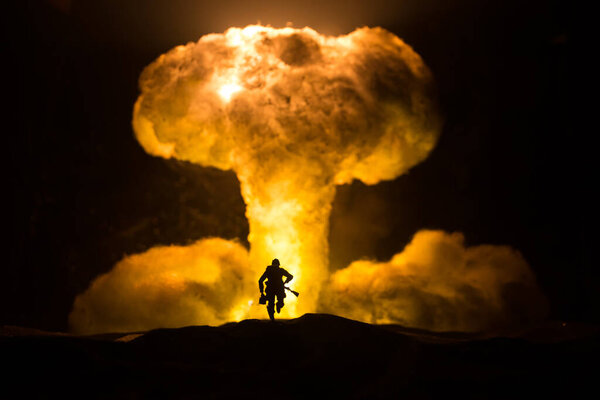 Nuclear war concept. Explosion of nuclear bomb. Creative artwork decoration in dark. Silhouette of soldier standing against giant mushroom cloud of atomic explosion. Selective focus