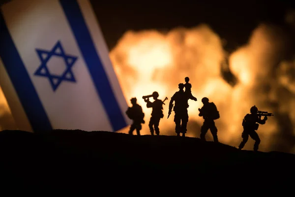 Israel small flag on burning dark background. Concept of crisis of war and political conflicts between nations. Silhouette of armed soldier against a Israel flag. Selective focus