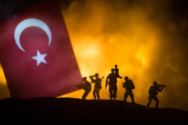 Yanan karanlık arka planda küçük bir hindi bayrağı. Savaş krizi kavramı ve uluslar arasındaki siyasi çatışmalar. Türk bayrağına karşı silahlı asker silueti. Seçici odak