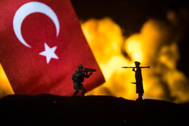 Yanan karanlık arka planda küçük bir hindi bayrağı. Savaş krizi kavramı ve uluslar arasındaki siyasi çatışmalar. Türk bayrağına karşı silahlı asker silueti. Seçici odak
